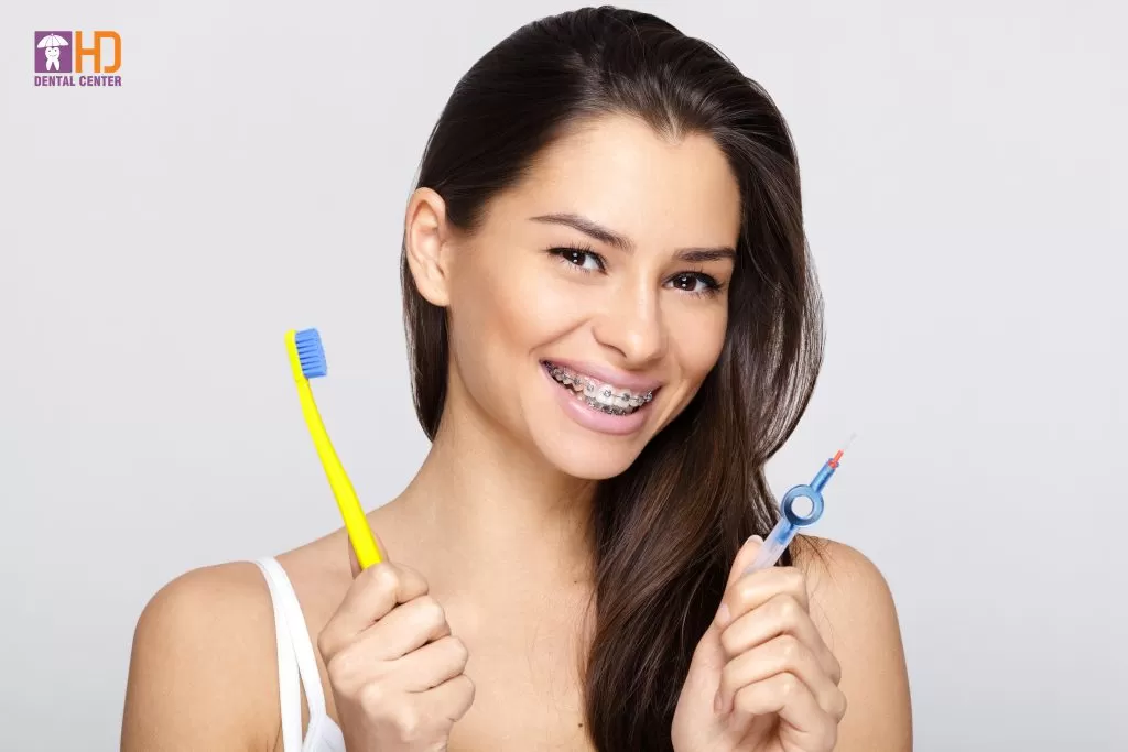 GIẢI PHÁP CHO NHỮNG NỖI LO KHI NIỀNG RĂNG Young woman with braces and toothbrush and braces brush cleaner